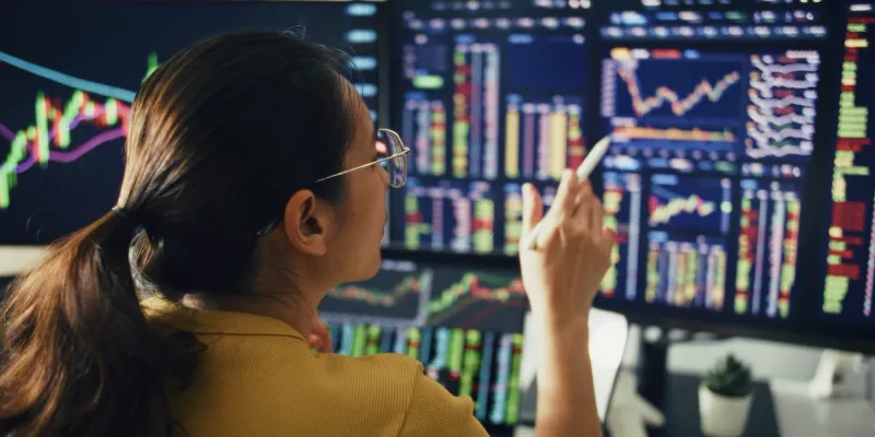 Person in yellow jacket analyzing stock market charts on multiple monitors.