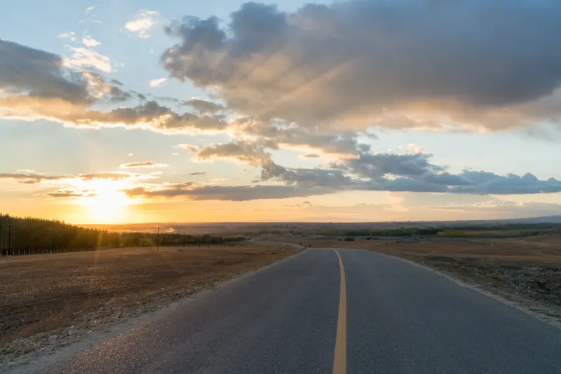 Sunset over an open road with clouds and a partly cloudy sky.