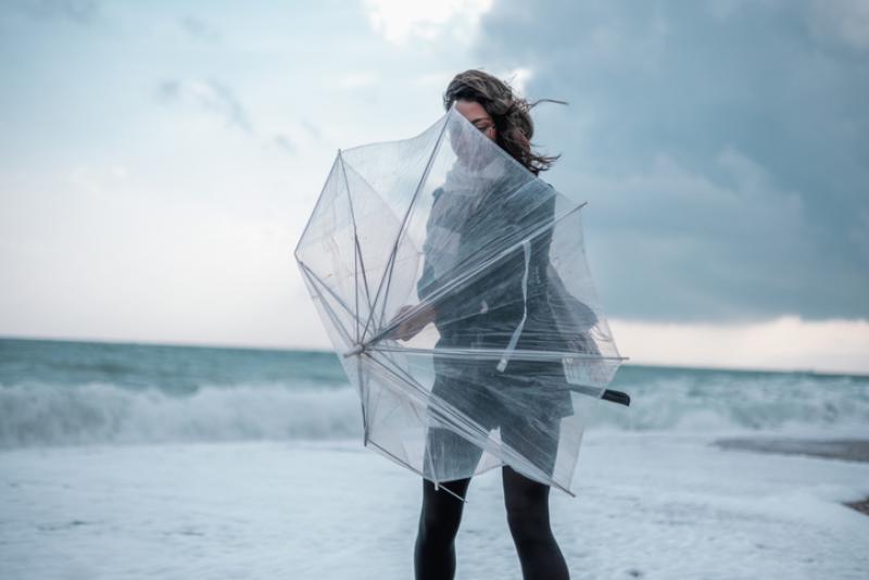 Sad young woman walking alone on the beach with umbrella in rainy weather Sad young woman walking alone on the beach with umbrella in rainy weather