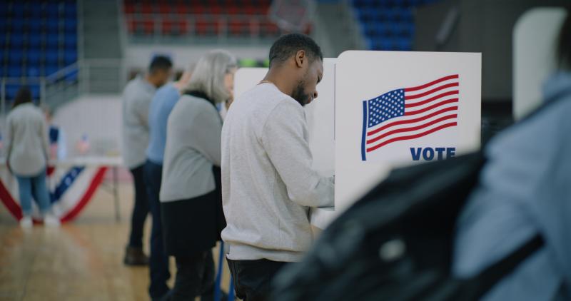 Elderly male voter with bulletin in hands comes to voting booth