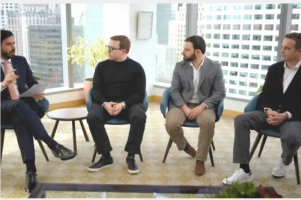 Four men seated on chairs in a modern office with large windows and cityscape background.