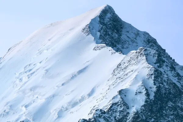 Snow-covered mountain peak with steep rocky face against a clear blue sky.