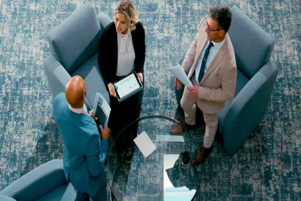 Three businesspeople in a discussion seated around a glass table in a modern office.