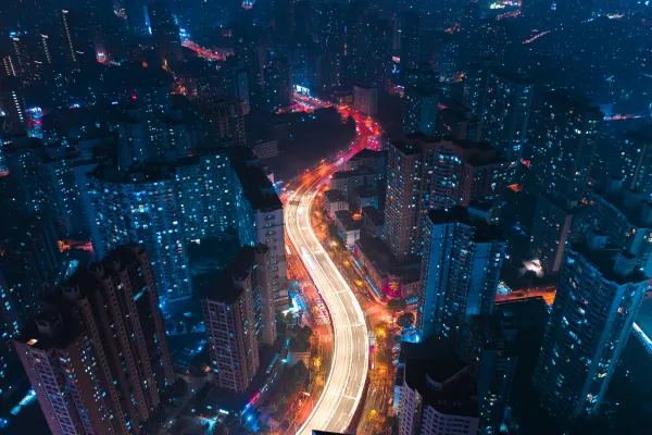 A cityscape at night with illuminated skyscrapers and a brightly lit highway winding through.
