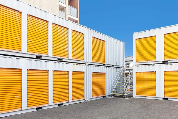 Stacked storage units with orange doors and yellow window shutters under a blue sky